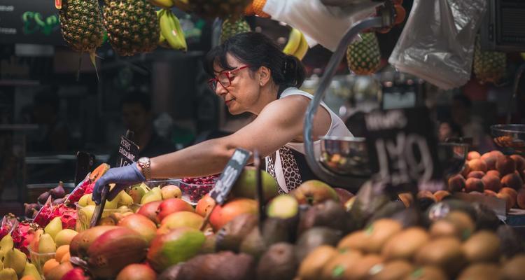 The image shows a food stand with a woman selling fruits.