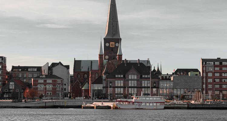 The image shows the Aarhus seafront, including boats, houses and a church.