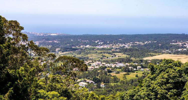 The image displays an aerial view on Lisbon Metropolitan Area, with towns, fields, forest and the sea in the background.