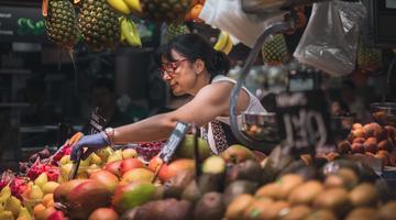 Photo by Daniel Angele on Unsplash The image shows a food stand with a woman selling fruits.