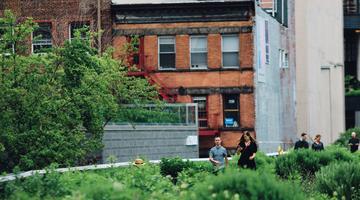 The image shows 4 people walking through a rooftop garden in an urban environment.
