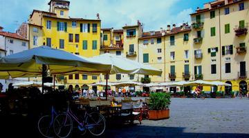 Photo by Marina T Alamanou on Unsplash The image shows the central square of the Italian town Lucca with sun umbrellas and seating places outside of restaurants.