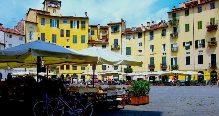 The image shows the central square of the Italian town Lucca with sun umbrellas and seating places outside of restaurants.